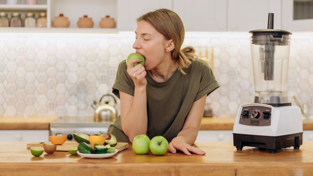Woman in kitchen eating fruit for a healthy diet