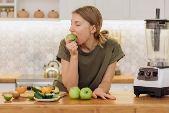 Woman in kitchen eating fruit for a healthy diet