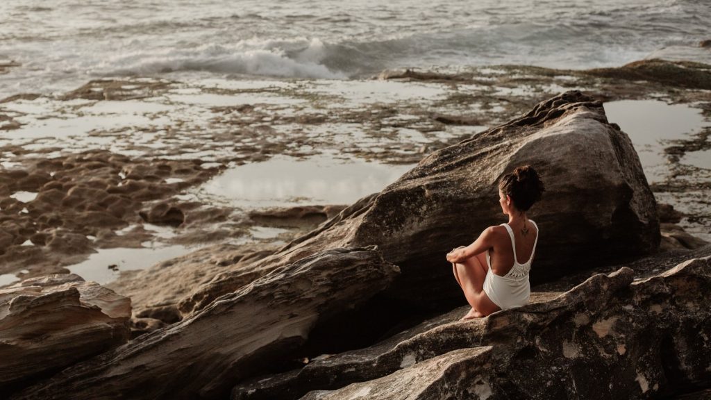 Woman sitting on rocks looking at the ocean