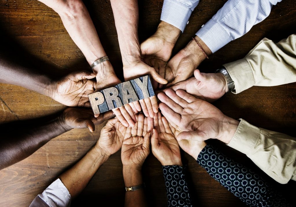 Many hands grabbing a woodblock that spells Pray